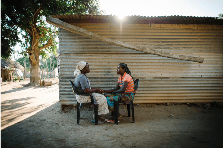 A woman involved in a Care Group program in Mozambique to share health information with her neighbor talks to another woman about TB. 