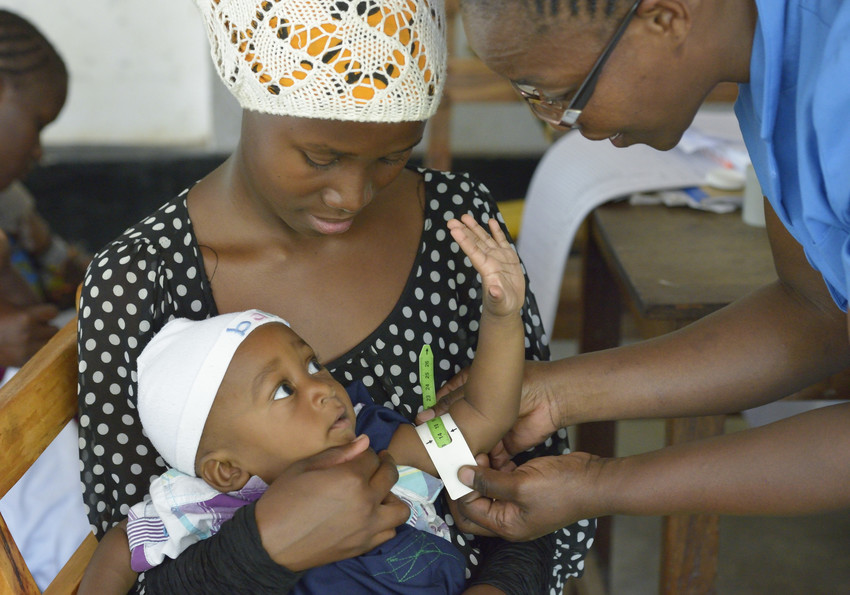A health worker examines a baby in a nutrition program while the mother holds the baby.