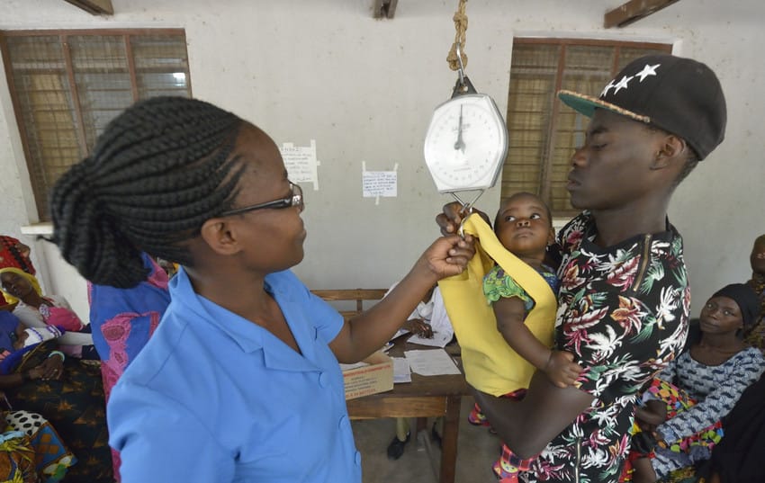 A man holds a baby to be weighed by a health worker in a nutrition program in Tanzania.