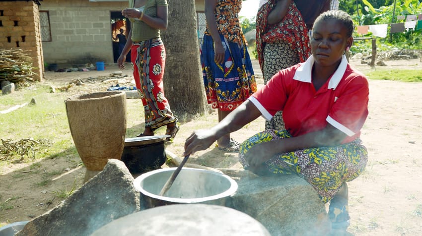 A woman stirs food cooking over a fire as part of a nutrition program in Tanzania