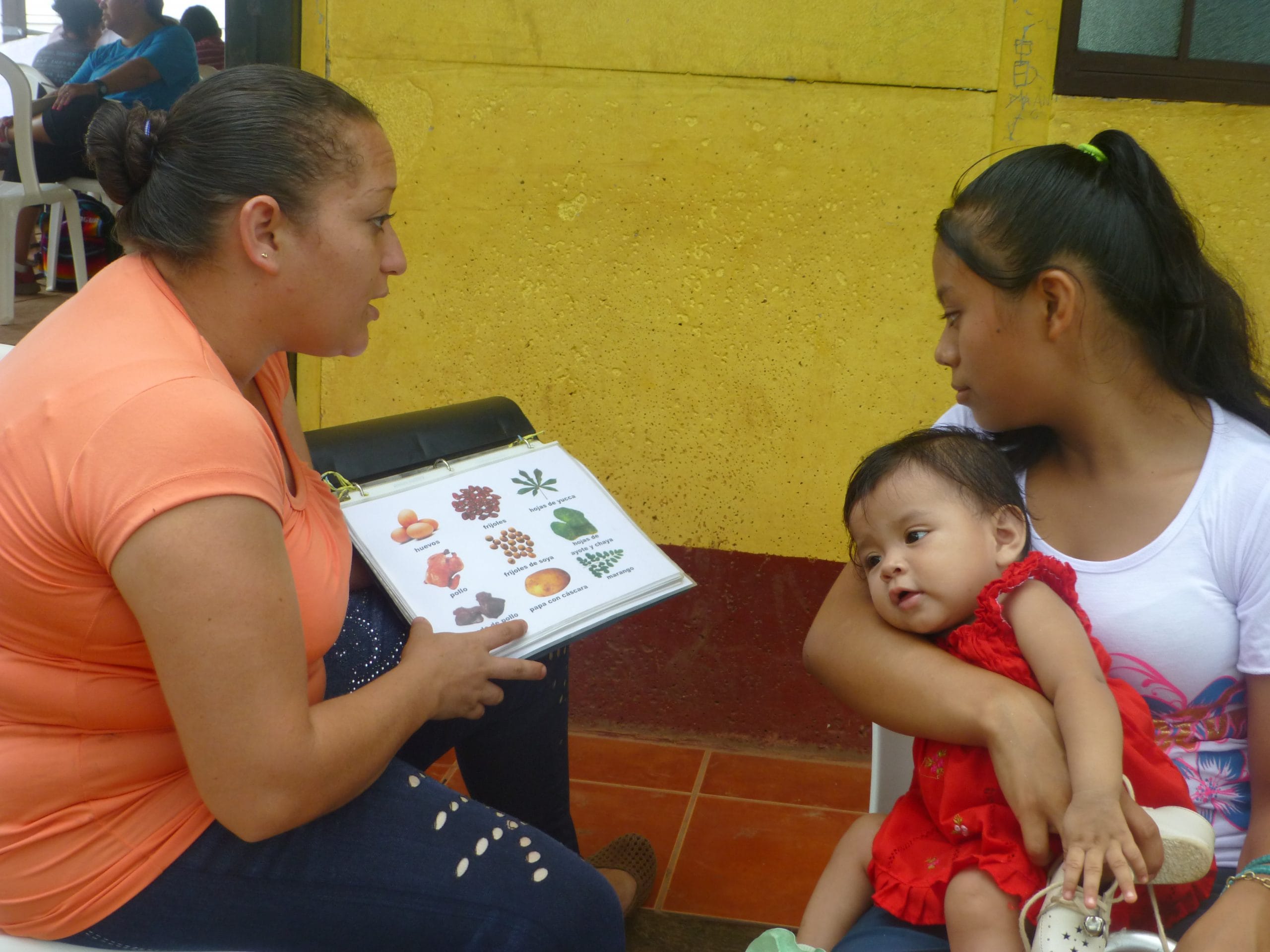 A community health worker shows health education information to a mother with a young child.