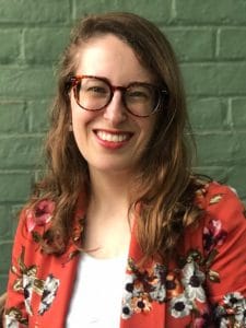 A woman, Cate Desjardins, is shown in front of a light colored brick wall.