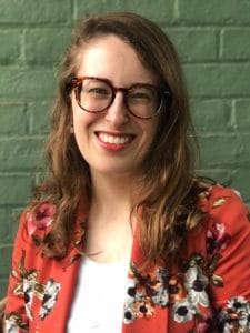 A woman, Cate Desjardins, is shown in front of a light colored brick wall. 