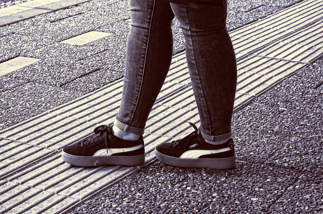 A woman's shoes are shown as she approaches tactile paving for the visually impaired on a road