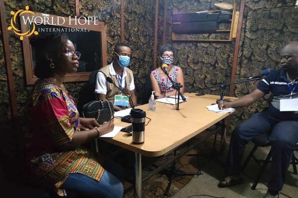 A group of people wearing masks to protect from COVID-19 infection sit at a table at a radio studio.