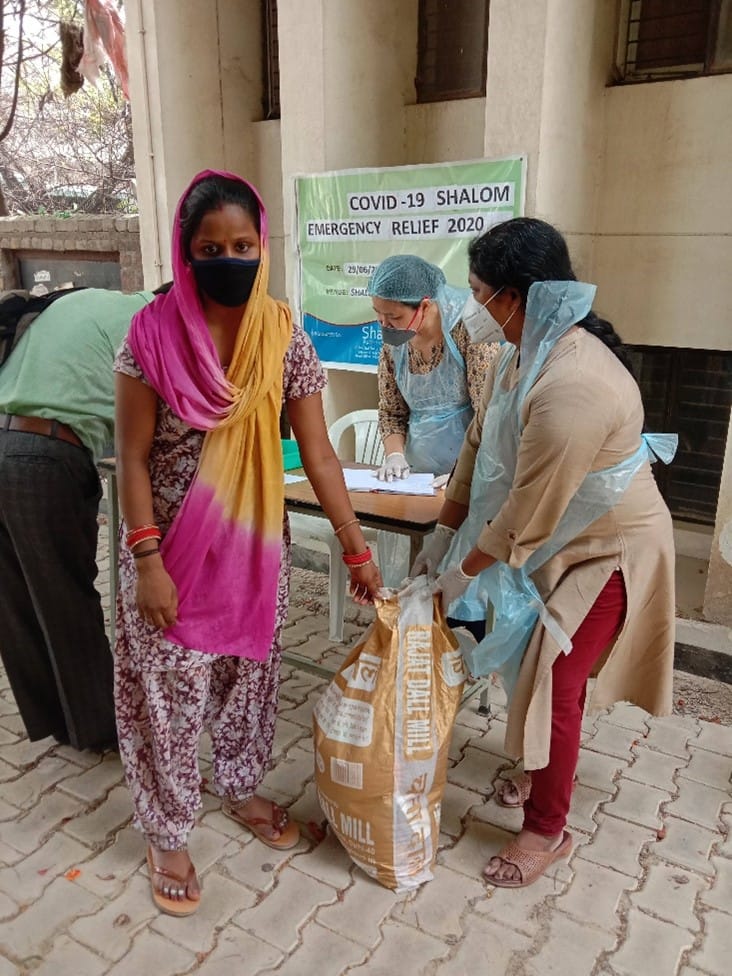 Two women stand next to a bag of food to distribute to people in need in India.