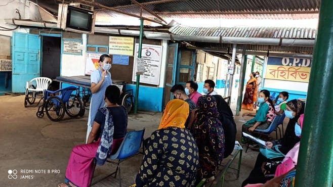 A nurse wearing a PPE mask talks to a group of people in India about COVID.