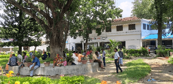 People sit around a tree in front of a health clinic in Bangladesh.