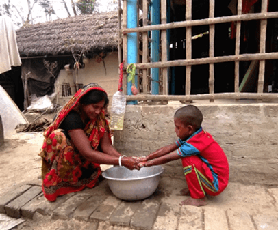 A mother and young child outside washing their hands with a large bowl.