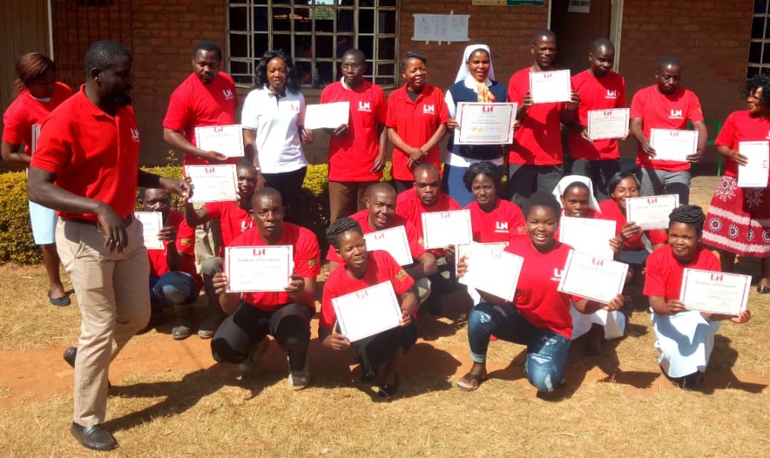 A group of people in matching red shirts display their health training certificates.