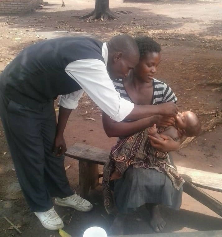 A man gives a child vitamin A orally while he lays on the lap of his mother in Malawi.