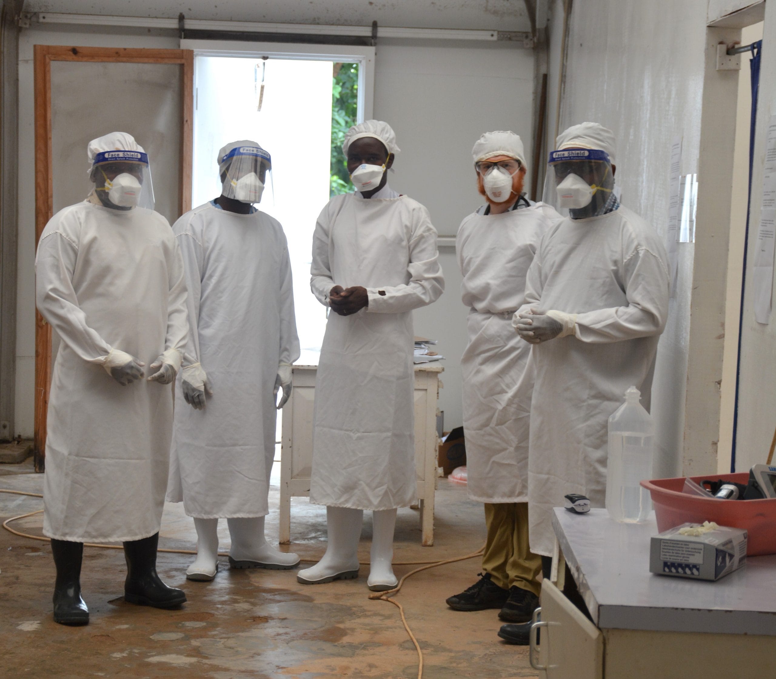 Five people in a health facility in full COVID personal protective great including masks and gloves.