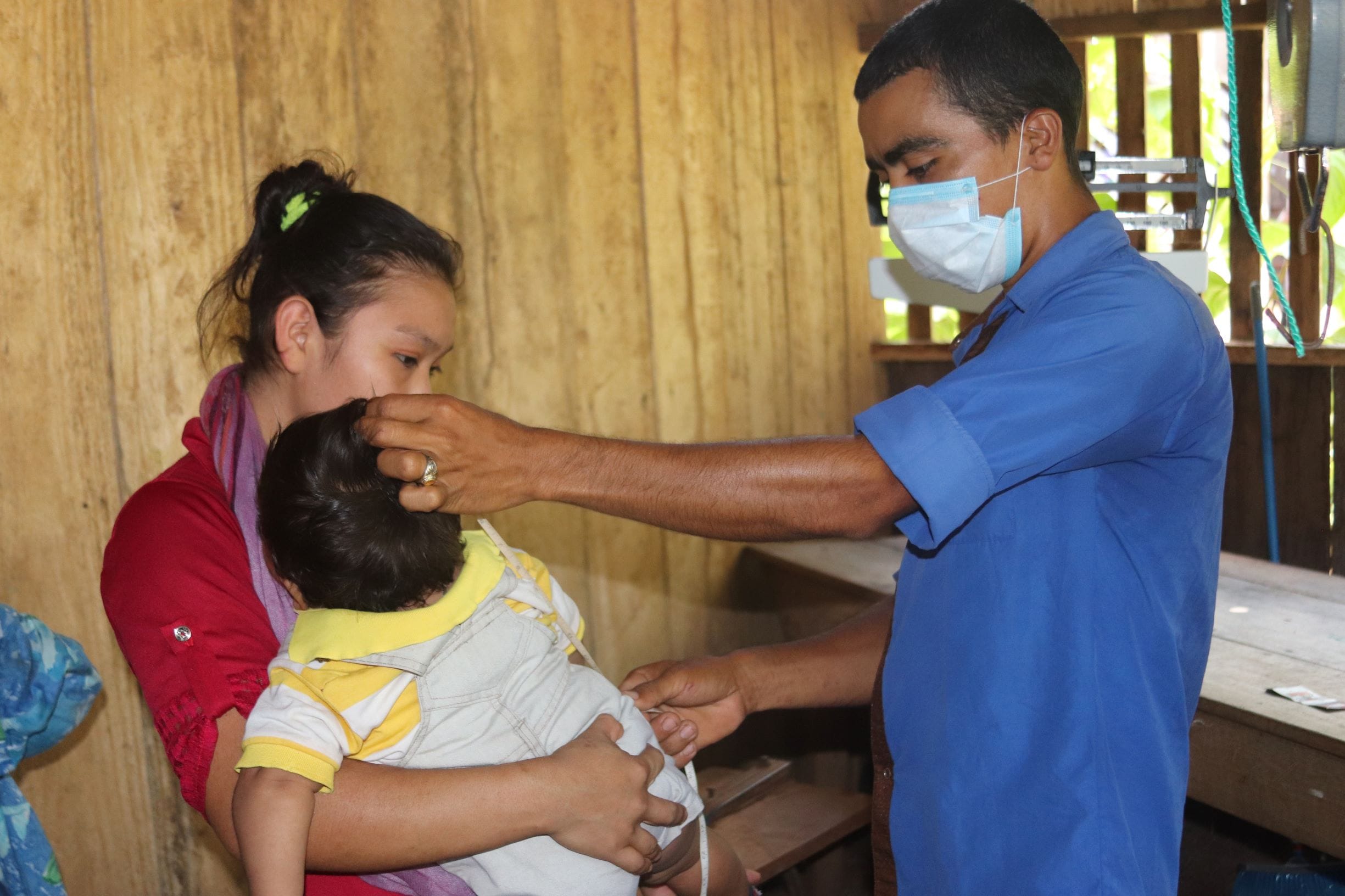 A community health worker measuring height of a baby.