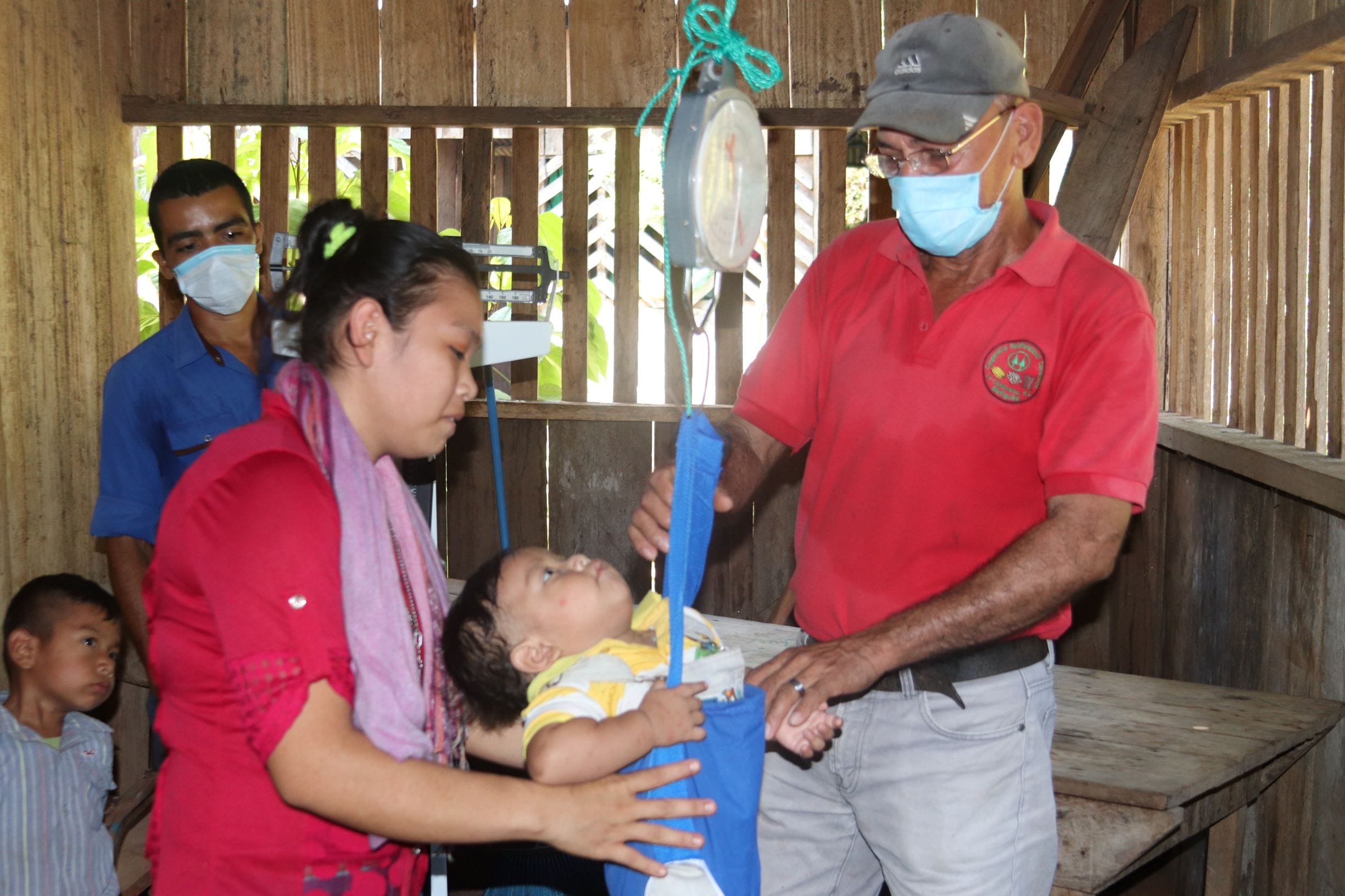 A health worker weighs a baby using a hanging scale.