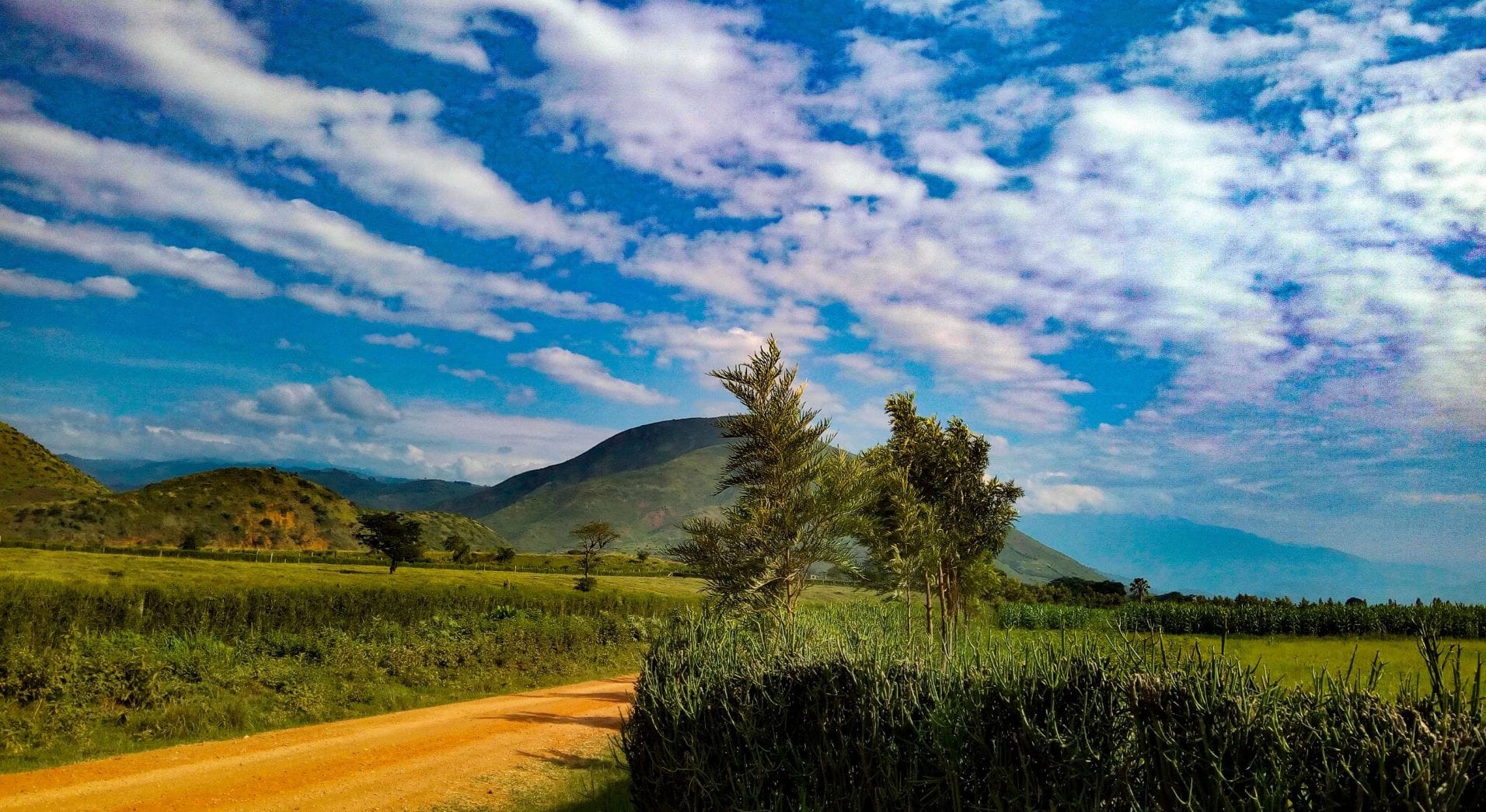 A mountain in Uganda under a bright blue sky with clouds.