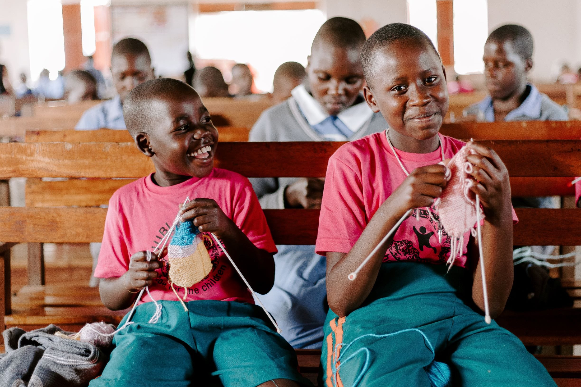 Two boys in matching shirts and shorts knit in a church in Uganda.