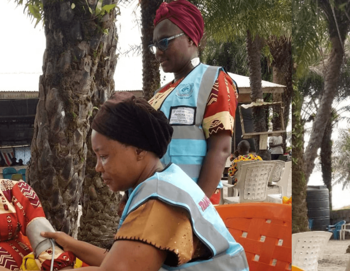 Two women in Liberia check the blood pressure of a church member at a health clinic held outside